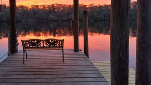 Eine Holzsteg mit einer Bank, der auf ruhiges Gewässer und eine bewaldete Landschaft bei Sonnenuntergang blickt.