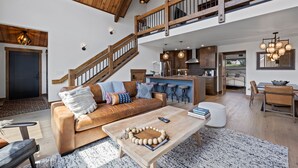A spacious living area with a high ceiling, wooden staircase, and a modern kitchen. - Estes Dream! End Unit with Patio, Indoor/Outdoor Fireplace and Jacuzzi (Estes Park)