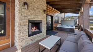 A covered outdoor patio with a stone fireplace, a sofa, and a TV. - Estes Dream! End Unit with Patio, Indoor/Outdoor Fireplace and Jacuzzi (Estes Park)