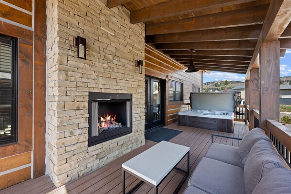 A covered outdoor patio with a stone fireplace, a sofa, and a TV. - Estes Dream! End Unit with Patio, Indoor/Outdoor Fireplace and Jacuzzi (Estes Park)
