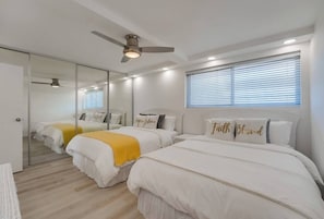A hotel room with two beds, a ceiling fan, a large mirror, and a window with blinds.