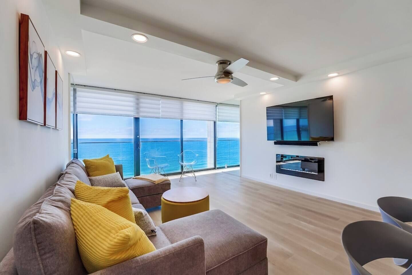A modern living room with a sofa, chairs, a TV, and a view of the ocean.
