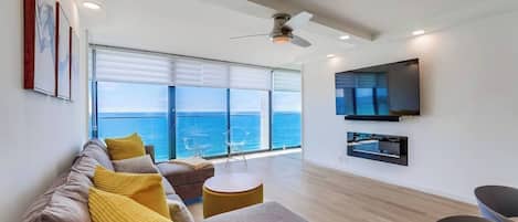 A modern living room with a sofa, chairs, a TV, and a view of the ocean.