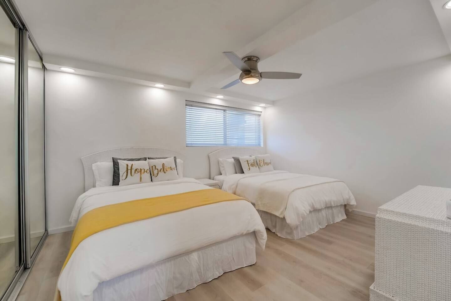 A bedroom with two beds, a ceiling fan, and a window with blinds.