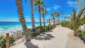 A coastal walkway lined with palm trees leading to a beach with clear blue water. - Modern 1bd Oceanfront view with parking and pool (San Diego)