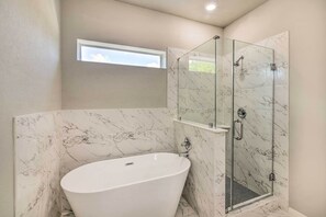 Un baño con una bañera independiente, ducha con mampara de vidrio y paredes de mármol.