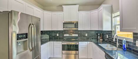 A modern kitchen with white cabinets, stainless steel appliances, a black tiled backsplash, and a wooden floor.