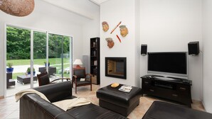 A modern living room with a large TV, comfortable seating, a bookshelf, and a view of the outdoors. - Les Villas de Fontenelles (Apremont)