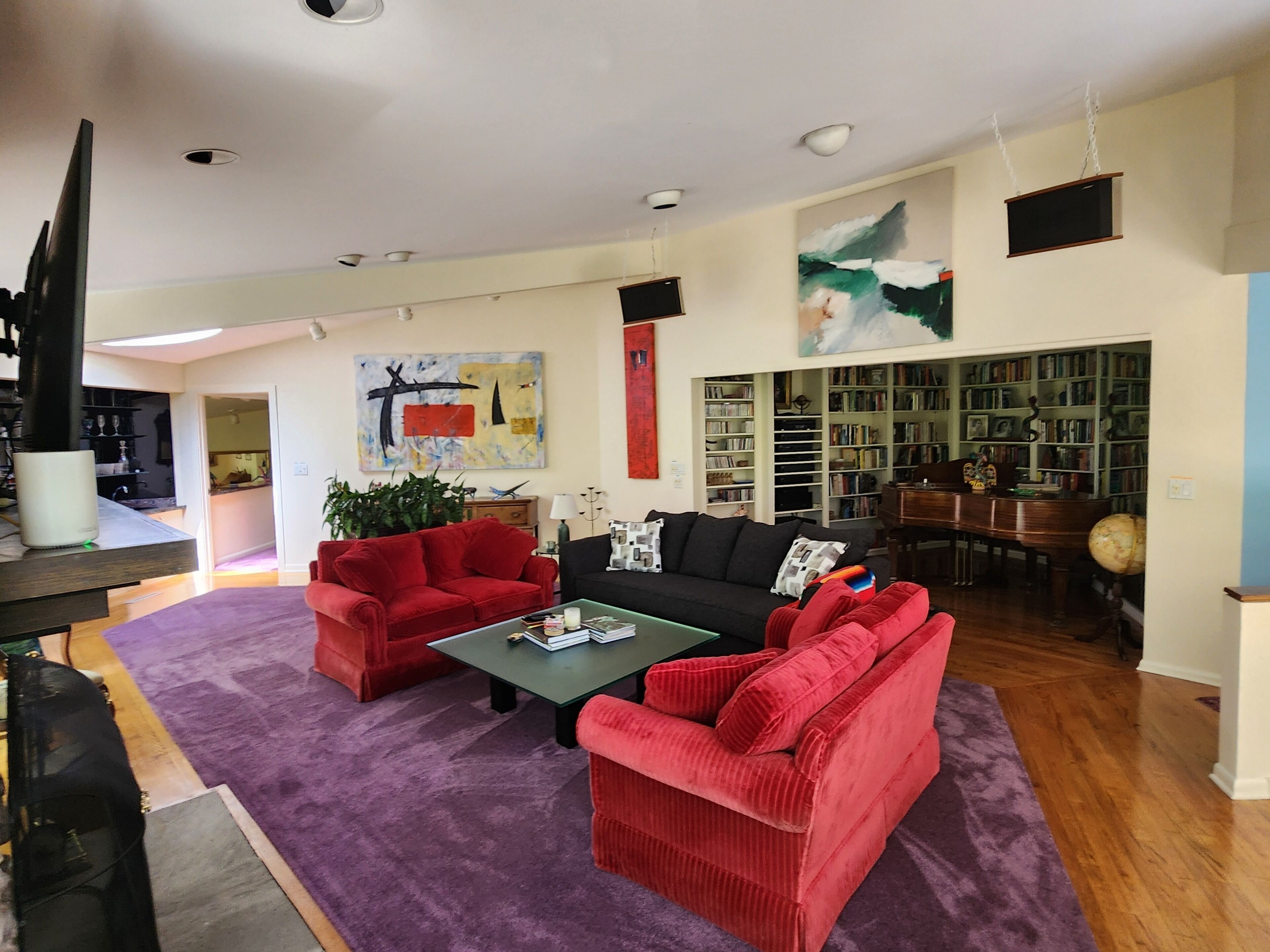 A spacious living room with a large coffee table, red sofas, a black sofa, and a bookshelf filled with books.