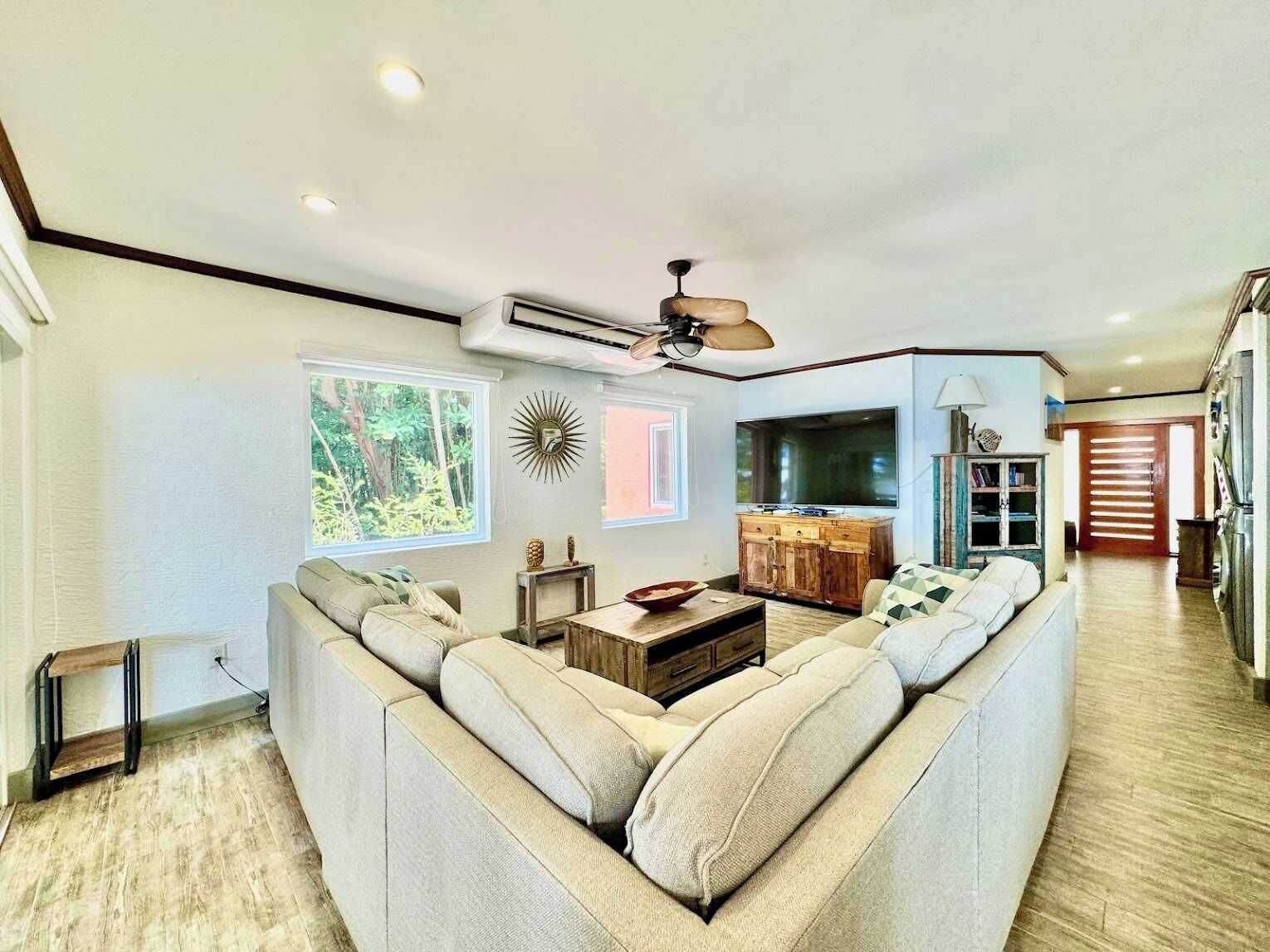 A living room with a sofa, a ceiling fan, and a TV.