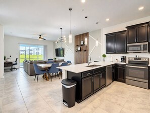A modern kitchen with dark cabinetry, a central island, and a dining area with blue chairs.
