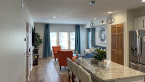 Une cuisine moderne dotée d’un plan de travail en granit, d’appareils électroménagers en acier inoxydable et d’un coin repas avec des chaises orange.