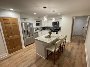 A modern kitchen with stainless steel appliances, a central island with bar stools, and a wooden floor. - Luxury King Suite—Steps from Mayo Clinic Hospital (Rochester)