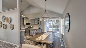 A modern kitchen with a central island, a dining area with a wooden table and chairs, and a large mirror on the wall. - Modern Flagstaff Retreat ~ 4 Mi to Downtown! (Flagstaff)