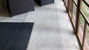 Varanda coberta com móveis de vime, janelas amplas e piso de concreto.