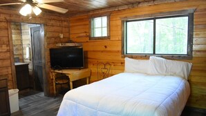 A log cabin room with a bed, a TV, a desk, and a window.