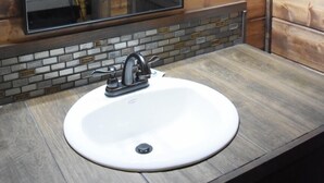 A bathroom with a wooden interior, a round sink with a modern faucet, and a mirror with a lighted frame.