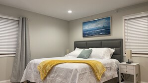 A bedroom with a bed, a nightstand, a painting, and a window with blinds. - Upscale King Suite—Steps from Mayo Clinic Hospital (Rochester)
