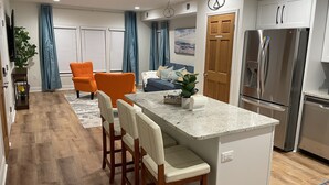A modern kitchen with a central island, wooden chairs, a refrigerator, and a dining area with a sofa. - Upscale King Suite—Steps from Mayo Clinic Hospital (Rochester)