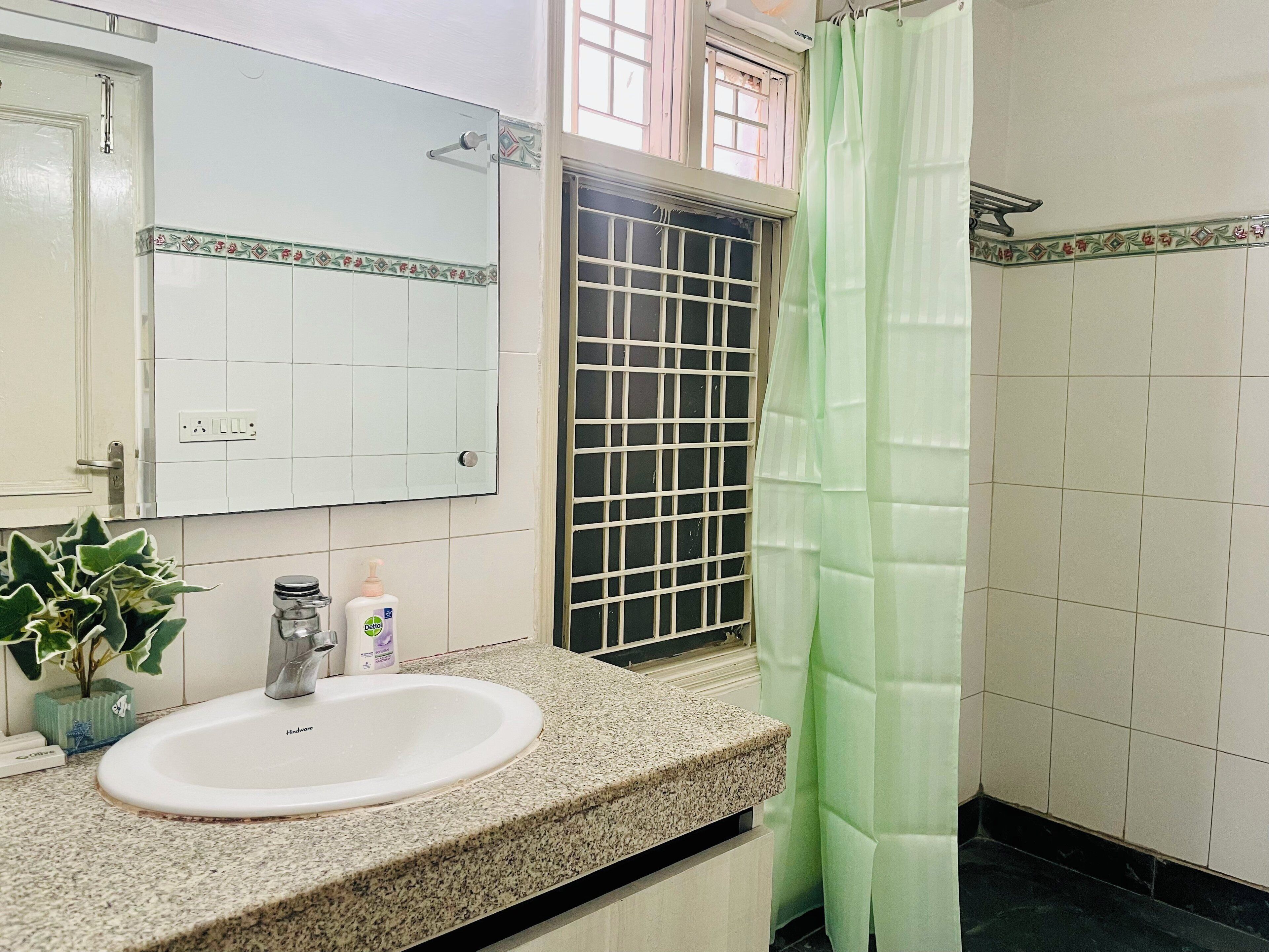 A bathroom with a granite countertop, a white sink, a mirror, a window with a metal grill, and a green shower curtain.