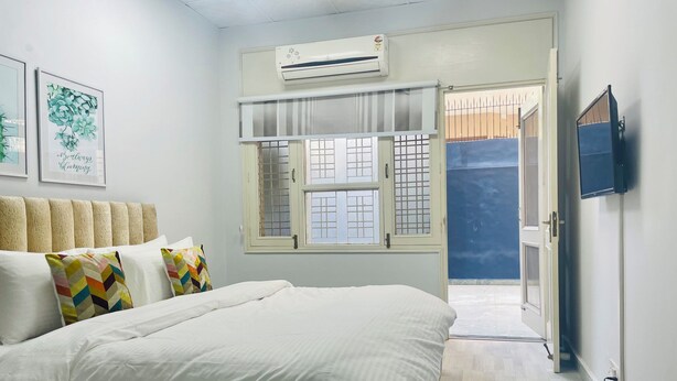 Une chambre à coucher avec un lit, des oreillers, une fenêtre, un appareil de climatisation et un téléviseur.