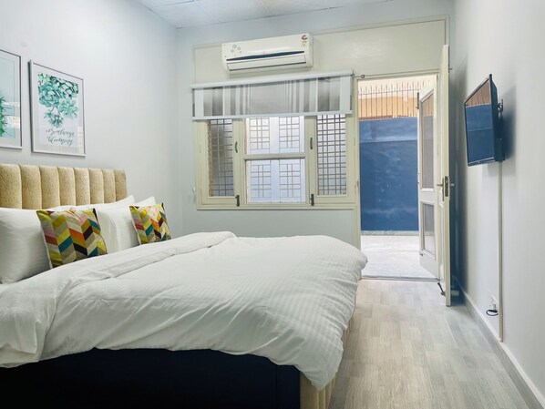Une chambre à coucher avec un lit, des oreillers, une fenêtre, un appareil de climatisation et un téléviseur.
