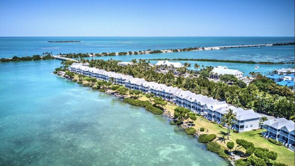 Vue aérienne d’un complexe hôtelier comportant plusieurs bâtiments le long d’une côte, avec une eau turquoise cristalline et une végétation luxuriante.