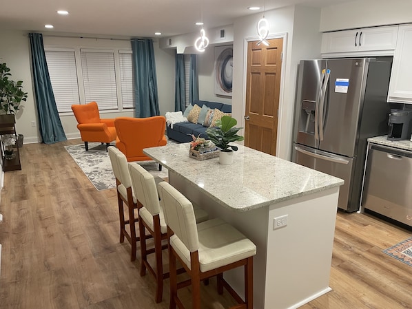 A modern kitchen with a central island, stainless steel appliances, and a seating area with orange chairs.