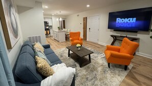 A living room with a sofa, two orange armchairs, a coffee table, and a flat-screen TV displaying "Roku Born". - Penthouse Suite—Steps from Mayo Clinic Hospital (Rochester)