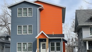 A multi-story residential building with a blue and orange facade, a front entrance with steps, and a driveway. - Penthouse Suite—Steps from Mayo Clinic Hospital (Rochester)