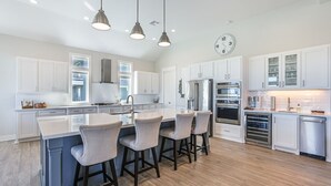 A spacious kitchen with white cabinetry, a central island with bar stools, stainless steel appliances, and pendant lighting. - SEASHELLS BY THE SEASHORE - Beautiful beachfront, sleeps 12! (Port Bolivar)