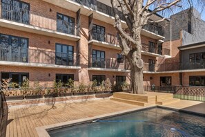 Un immeuble résidentiel à plusieurs étages doté d’une piscine, de balcons et d’un arbre dans la cour.