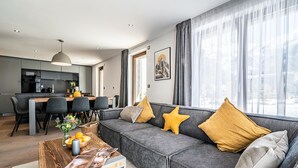 A modern living room with a grey sofa, yellow and grey cushions, a wooden coffee table, and a dining area with a grey table and chairs. - EYONG - Premium apartment with sauna and hot tub (Chamonix-Mont-Blanc)