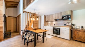 Una cocina moderna con armarios de madera, un comedor con mesa y sillas de madera, y una escalera con vigas a la vista.