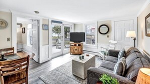 A living room with a TV, sofa, coffee table, and dining area. - The Breakwaters Hyannis - Your Home Away From Home! RPAM046 (Hyannis)
