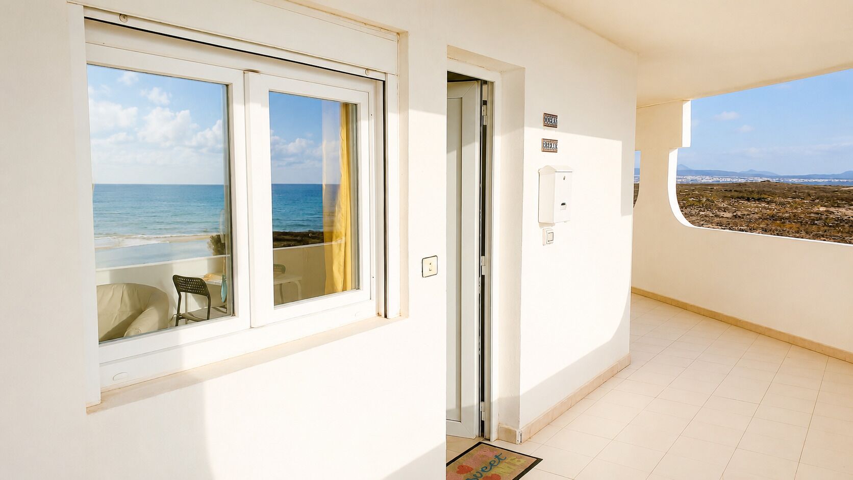 Een balkon met uitzicht op zee, een deur en een lichtschakelaar aan de muur.