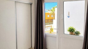 Une pièce dotée d’une porte coulissante, d’une fenêtre donnant sur des immeubles et d’une petite plante en pot posée sur le rebord de la fenêtre.