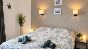 A bed with a floral bedspread, two wall-mounted lamps, a star decoration, and a potted plant. - Ocean View Apartment • Sunny Balcony • Near the Coast (Antigua)