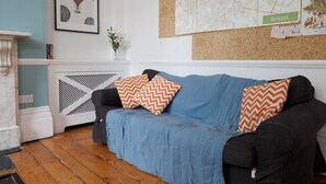 A living room with a blue sofa, two patterned cushions, a framed artwork, a map, and a small plant.