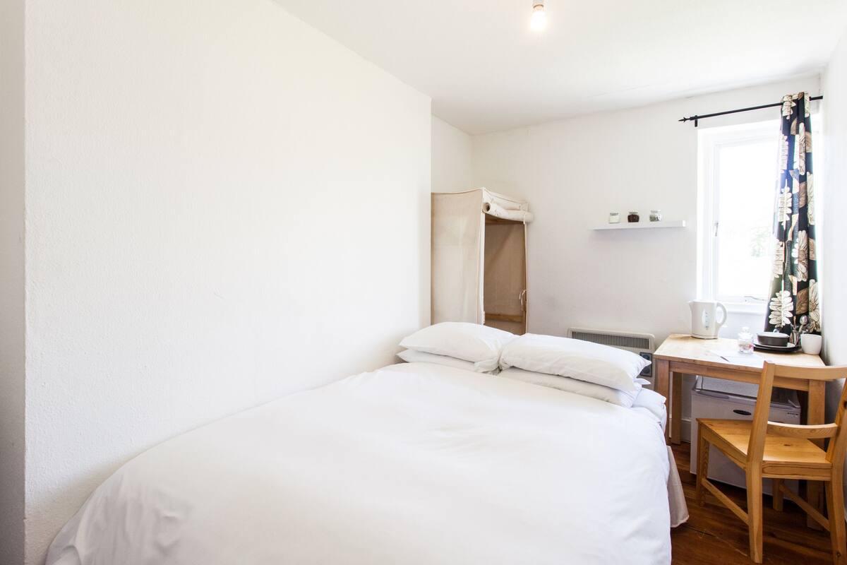 Een slaapkamer met een bed, een houten bureau, een stoel, een radiator en een raam met gordijnen.