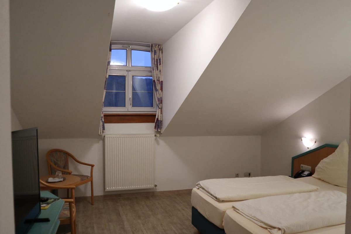 A room with a bed, a desk, a chair, a window with curtains, and a radiator.