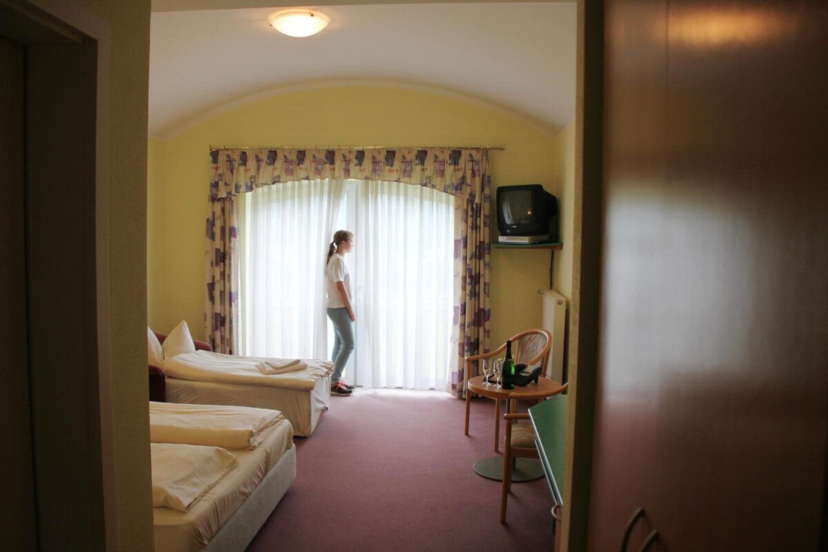 A hotel room with two single beds, a television on a stand, and a chair with a bottle and glasses.