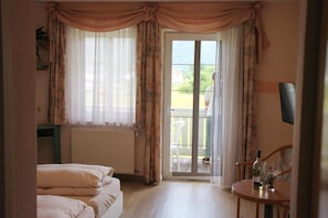 Ein Hotelzimmer mit Bett, Sessel, Tisch mit Flasche und Glas sowie Blick ins Freie durch eine Schiebetür.