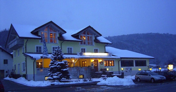 Un grand immeuble à plusieurs étages, dont le toit est recouvert de neige et l’entrée est illuminée.