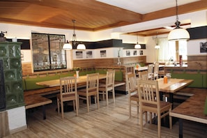 Un restaurant avec des tables et des chaises en bois, un coin salon avec des banquettes vertes et un mur orné de photographies en noir et blanc.