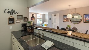 A modern kitchen with a granite countertop, stainless steel sink, and a coffee-themed decor. - The Downtown Trifecta |Large & Unique Lodging | Perfect for Group Stays |Main St |Parking Included (Lake Geneva)