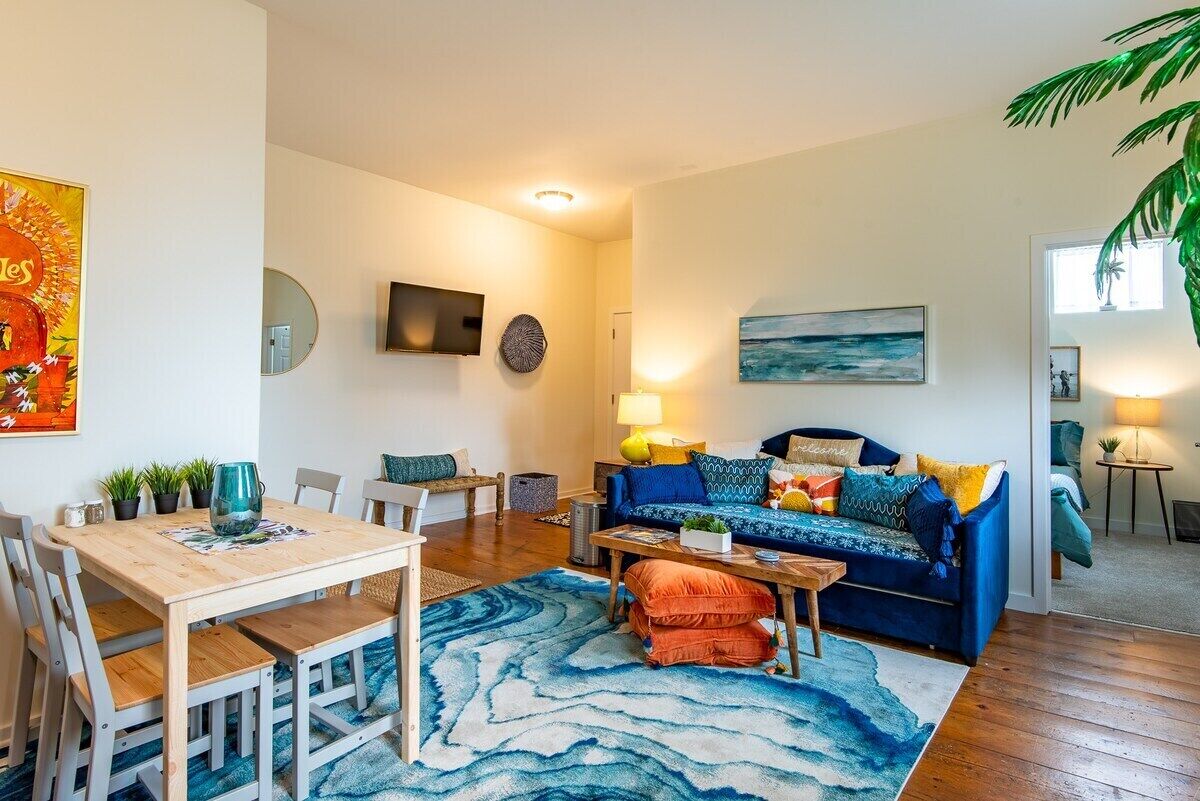 A living room with a wooden dining table, blue sofa, and a large abstract rug.