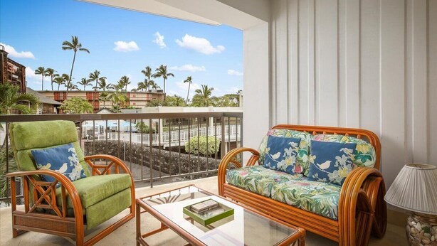 A balcony with wicker furniture, a view of palm trees, and a clear sky.