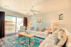 Relax in this inviting living room with a sofa set, coffee table, and patterned rug, offering a view of the outside through the large window.