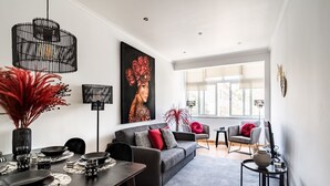 A modern living room with a grey sofa, black and red cushions, a dining table set with plates and glasses, and a large abstract painting on the wall. - Sapphire Apartment, AC, Wifi !new! (Lisboa)
